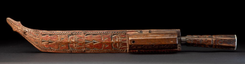 Paiwan tribe hunting knife with a sheath carved with a standing figure and human faces on the side. The hilt is made of carved wood.
