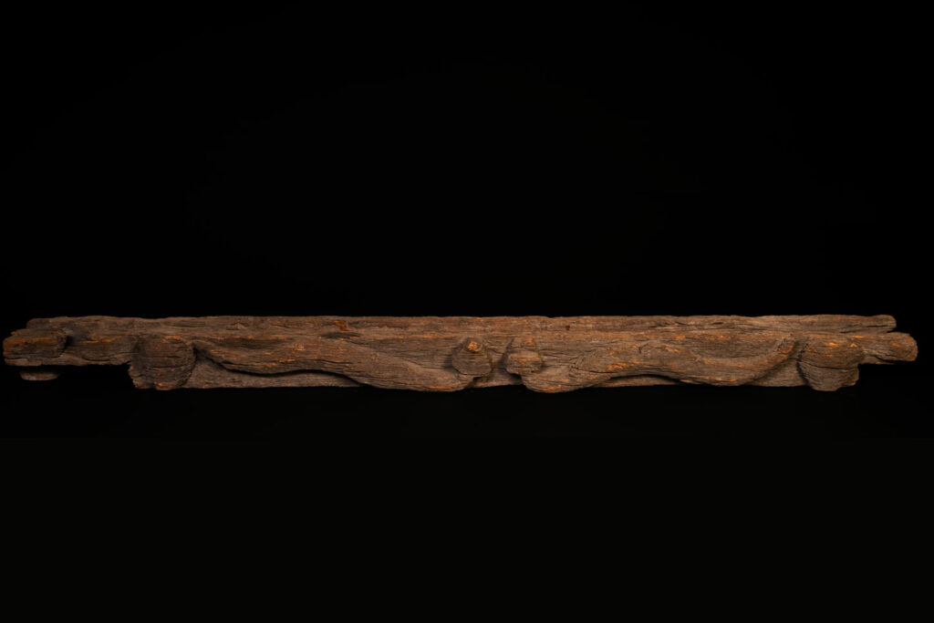 19th-century door lintel from the Paiwan tribe, carved with a pair of snakes facing each other and two human faces on either side. This Paiwan panel is heavily eroded and was probably placed above the entrance, exposed to the elements.