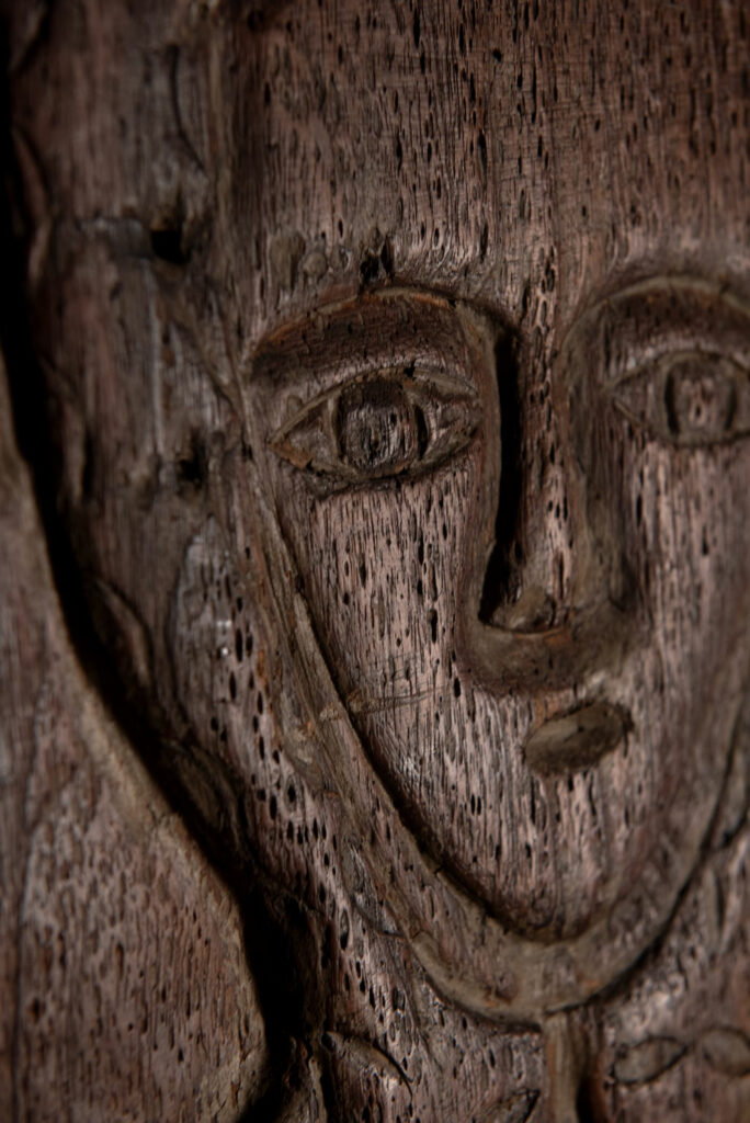 Ancestor panel from the Paiwan tribe, carved with a figure wearing a hat adorned with eagle feathers, a symbol of valor. His face is encircled by two snakes merging into one, and flanked by two additional sacred snakes on each side.
