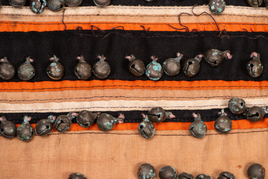 Pair of women’s legging from the Ami tribe, made of pink cotton fabric with orange and black stripes, sewn with ten rows of small bells. The bottom of each piece is adorned with green woolen knots. Such ankle ornaments were worn by women during ceremonies and festivals. This pair is estimated to date from the 1950s.