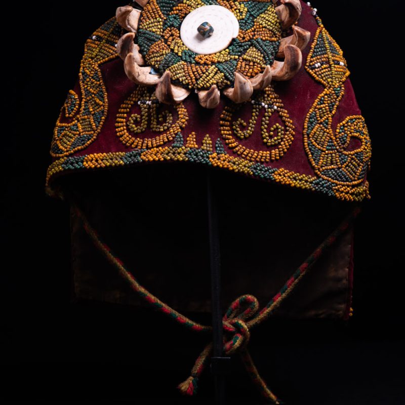 Paiwan tribe: ceremonial men's hat made of velvet, adorned with beadwork forming sacred snakes, and featuring a central rosette decorated with a round shell and boar tusks.
