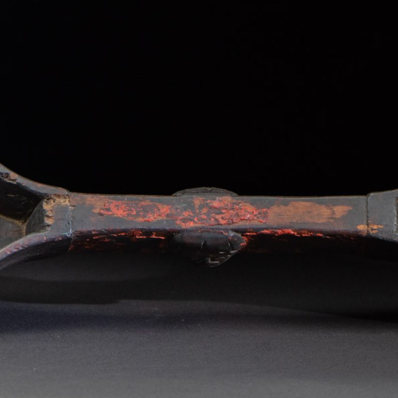 This linked cup from the Paiwan tribe features a diamond-shaped mouth and a central handle adorned with a carved human head. It is decorated with traditional black and red pigments.