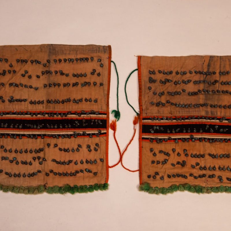 Pair of women’s legging from the Ami tribe, made of pink cotton fabric with orange and black stripes, sewn with ten rows of small bells. The bottom of each piece is adorned with green woolen knots. Such ankle ornaments were worn by women during ceremonies and festivals. This pair is estimated to date from the 1950s.