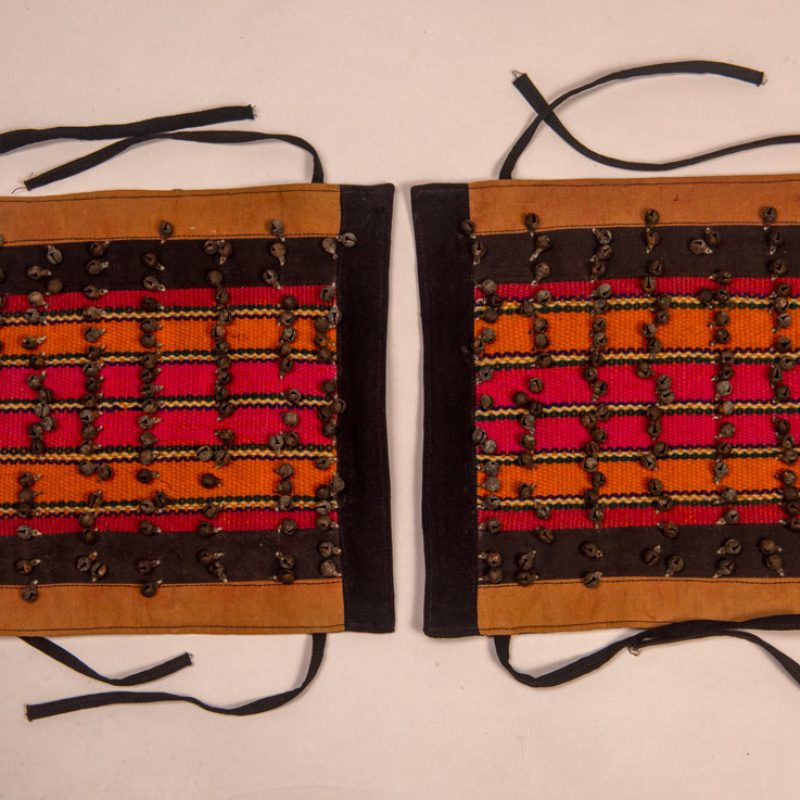 Antique Paiwan tribe women’s leggings made of red wool with black cotton panels and vertical stripes in pink, yellow, and orange. This traditional pair features eight rows of small copper bells and black cotton straps for tying around the calves. Such square leggings were worn over skirts to expose the lower legs and were decorated only by noblewomen. A rare example of formal Paiwan ceremonial wear from Taiwan's Indigenous heritage.