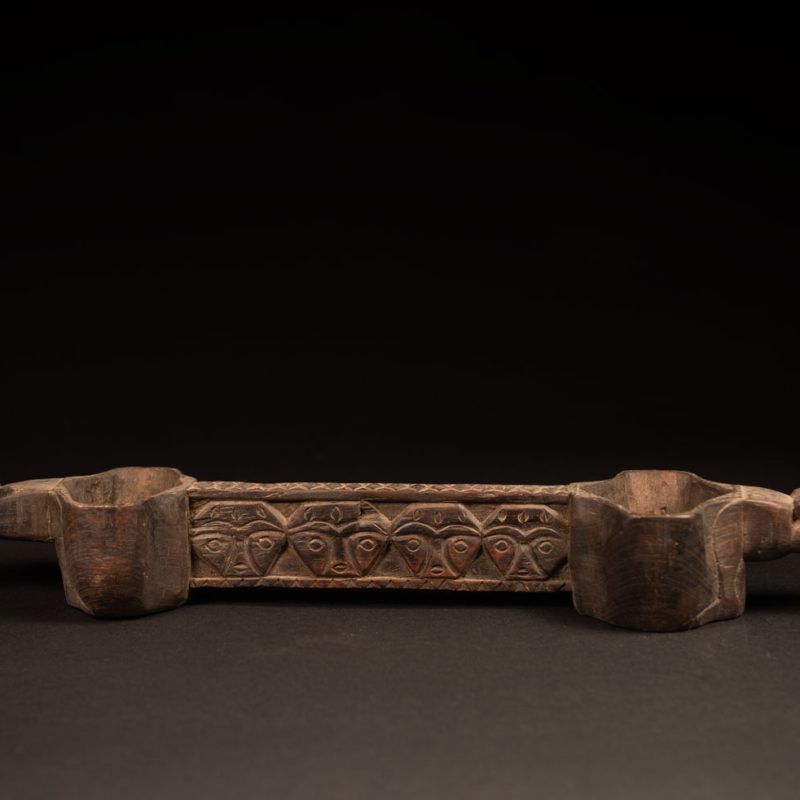 This drinking cup from paiwan features two beautifully carved handles, each depicting an ancestor holding the drinking cup between his thighs. The center of the double cup is carved with four human faces and a decorative frieze. The entire piece is made of natural wood.