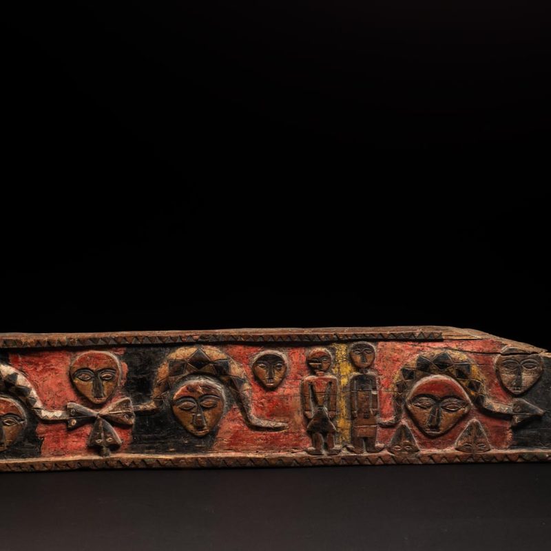 19th-century door lintel from the Paiwan tribe, carved with human heads topped by sacred snakes, along with two standing figures, likely a couple. This Paiwan lintel is painted in black, red, and yellow.