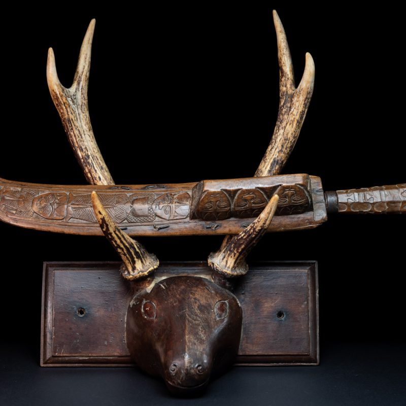 Paiwan tribe hunting knife with a sheath carved with a standing figure and human faces on the side. The hilt is made of carved wood.