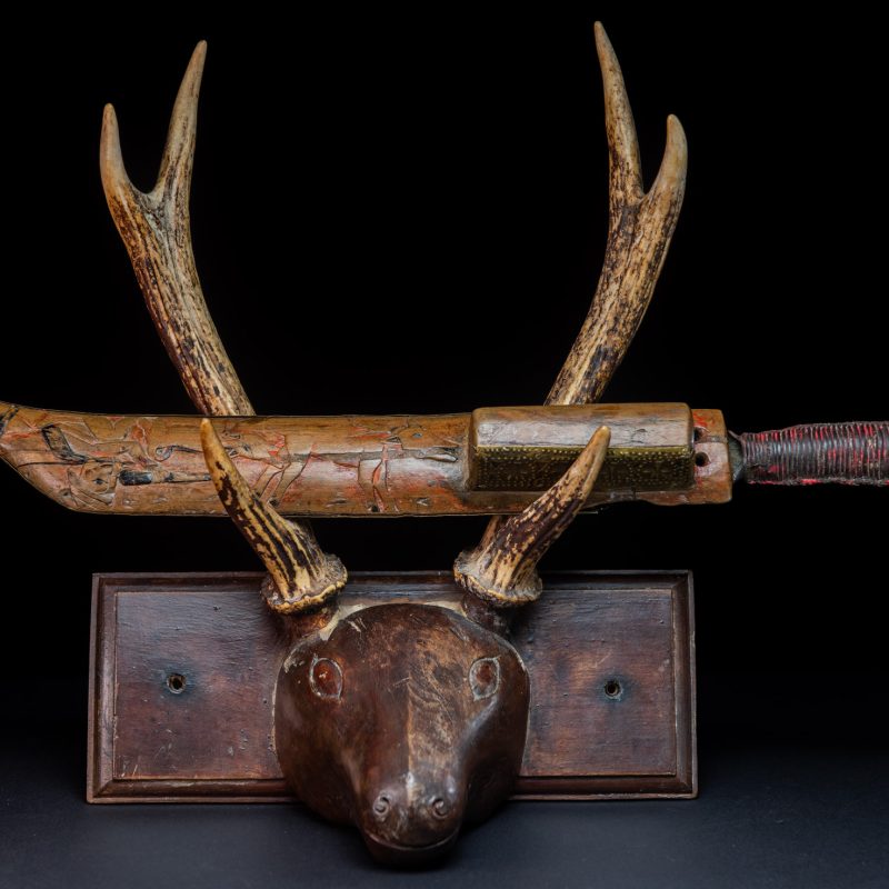 Hunting sword from the Paiwan tribe, with a sheath carved with a scene of a hunter accompanied by his dog shooting at deer. The sides and top of the sheath are covered with brass sheets finely embossed with human head motifs. The sword is made in one piece with the handle, which is wrapped in red-stained rattan.