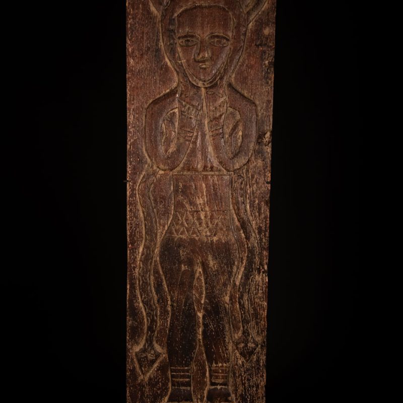 Ancestor panel from the Paiwan tribe, carved with a figure wearing a hat adorned with eagle feathers, a symbol of valor. His face is encircled by two snakes merging into one, and flanked by two additional sacred snakes on each side.