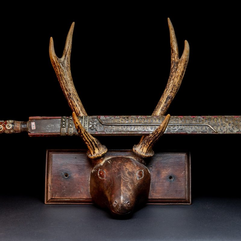 Ancient ceremonial long sword from the Rukai tribe. The back of the sheath is painted red and inlaid with finely engraved snakes in brass sheet. The top is also covered with an engraved brass plate. The very long blade of this Rukai sword features a handle in the Rukai style, decorated with small flower-shaped motifs and aluminum wire. The guard of the sword is made from a Japanese coin.